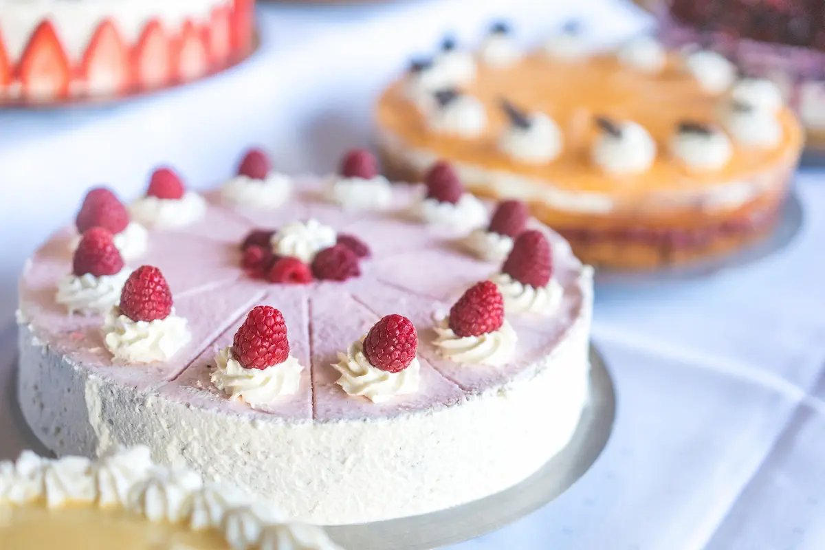 "Eine Auswahl an feinen Torten auf dem Kuchenbuffet im Kuckucks-Nest: Im Vordergrund steht eine angeschnittene Himbeertorte, die mit Sahnetupfen und frischen Himbeeren verziert ist."